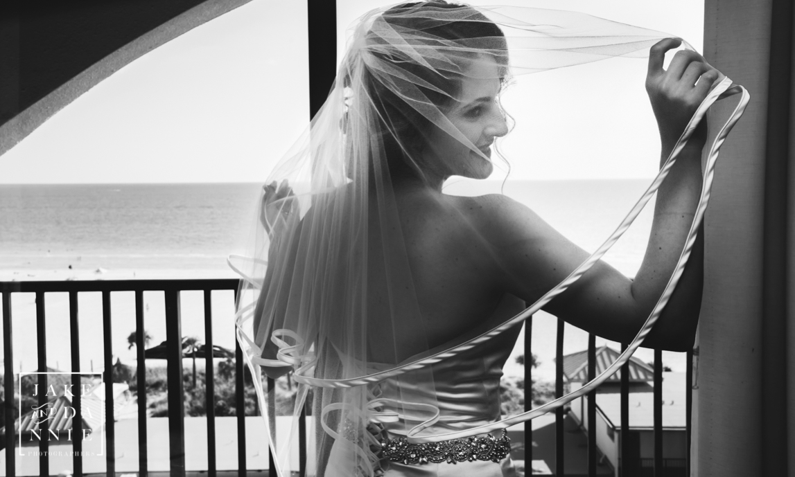 Beautiful bride looking through her veil with the beach out her window.