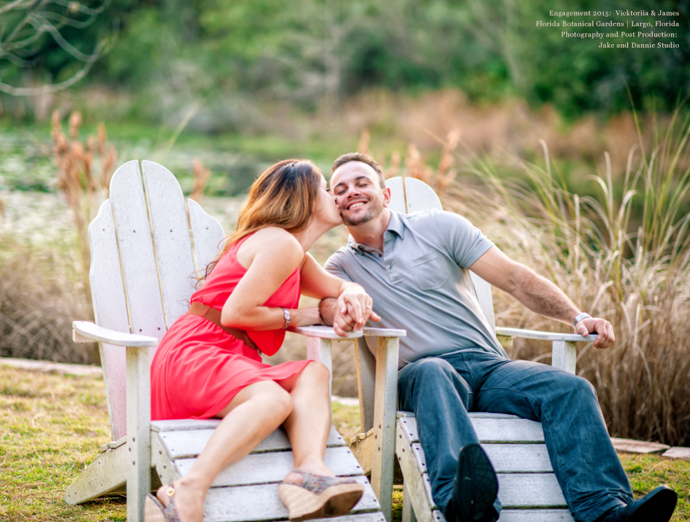 Engaged couple enjoys a rest in some white lawn chairs.  How about a kiss on the cheek?