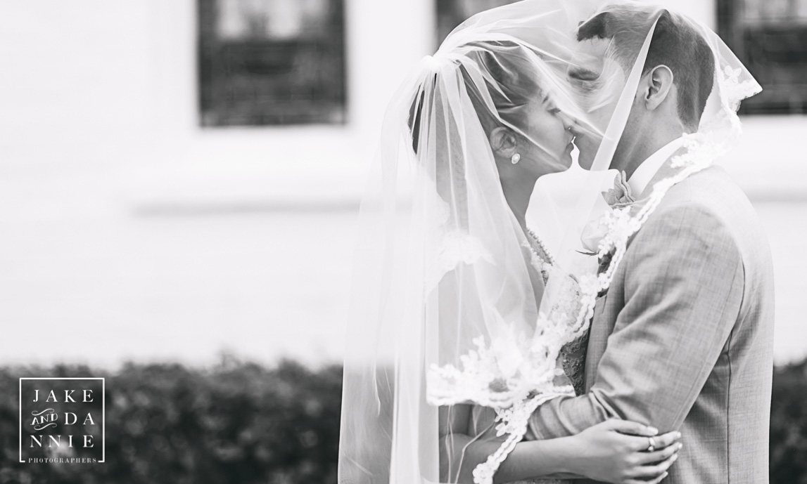 Black and white of bride and groom kissing under veil