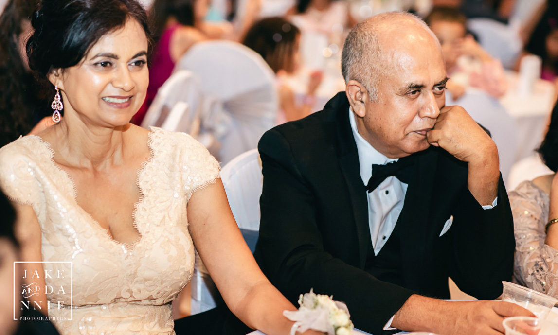 Bride's parents sit together at wedding reception.