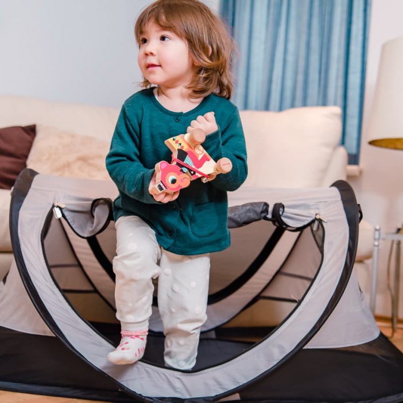 Toddler playing outside her Kidco Peapod Plus Baby Travel Tent.