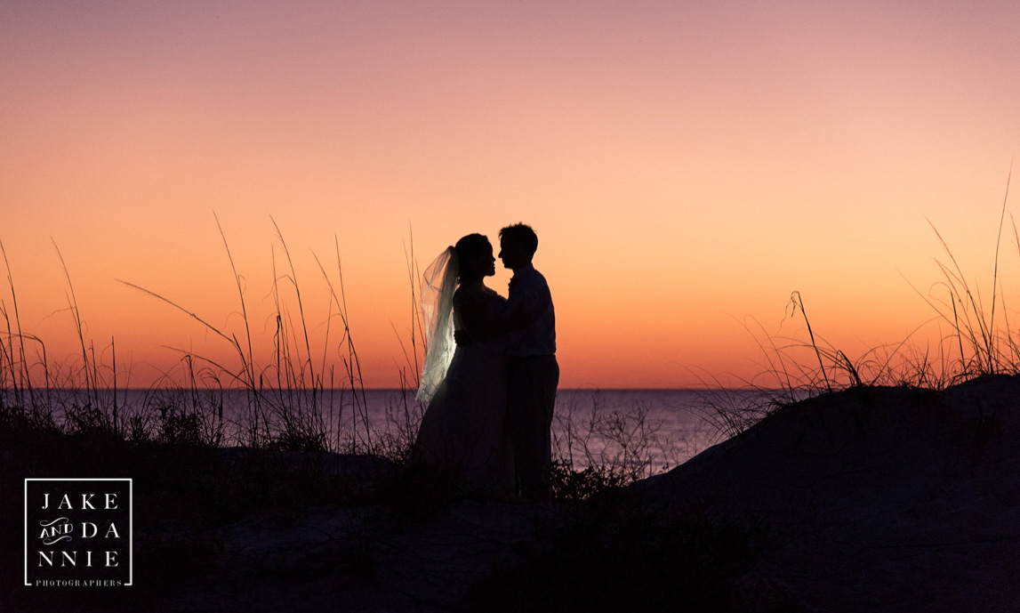 The bride and groom silhouetted against the sunset on the dunes near the beach