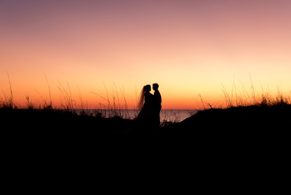 Bride and Groom share a romantic moment on the dunes near the beach at sunset