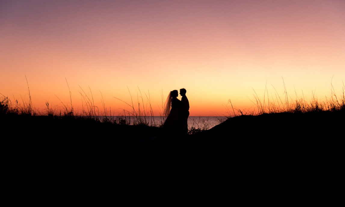 Bride and Groom share a romantic moment on the dunes near the beach at sunset
