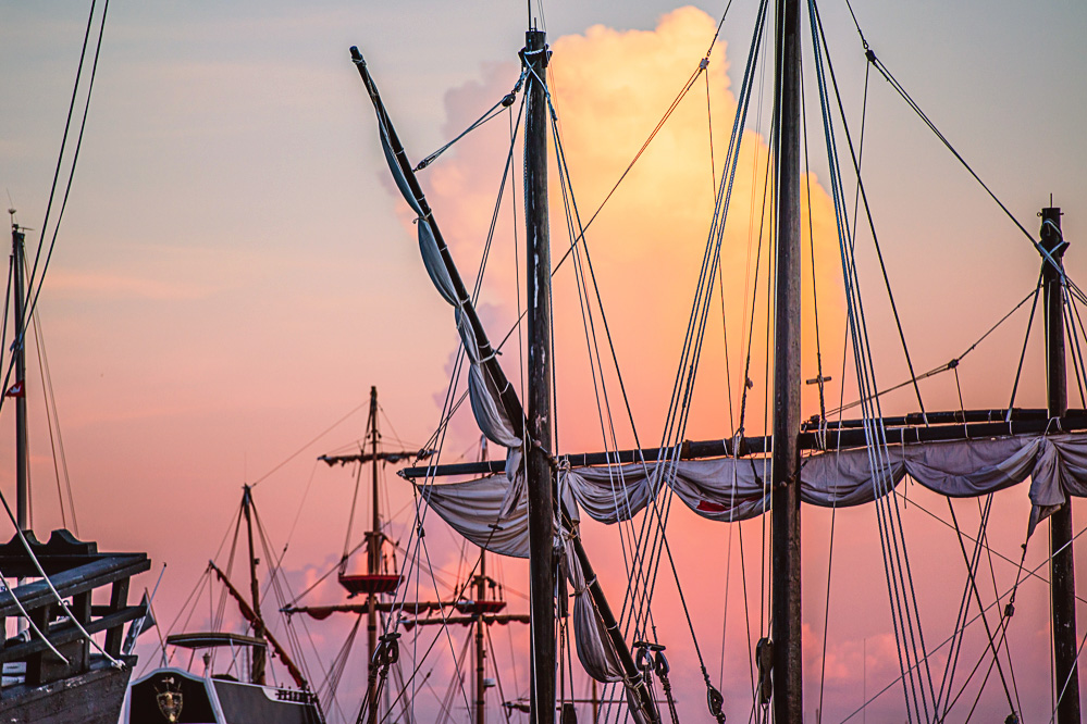 The masts of the tourist pirate ships with a beautiful cloud in the background at sunset