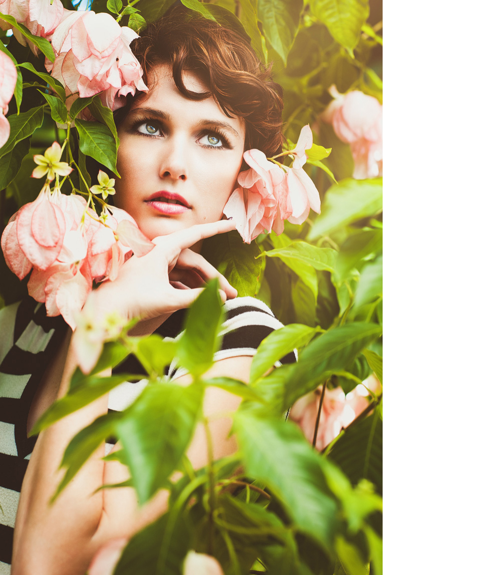 Woman with red hair and beautiful eyes hides among pink flowers