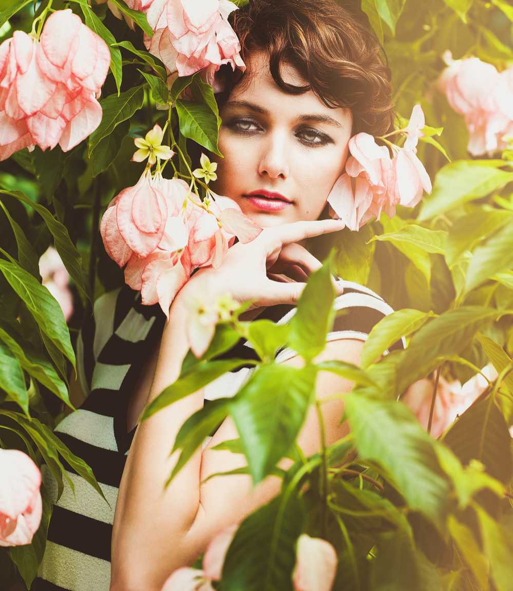 A flowering bush conceals a woman in a black and white dress