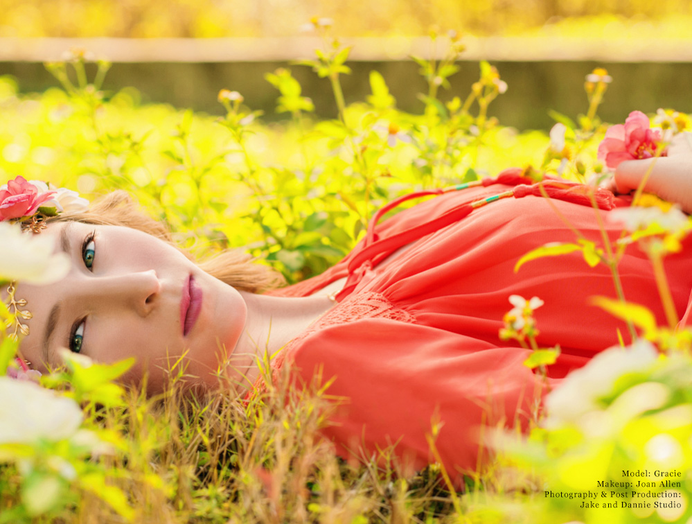 Headshot of girl in pink dress and headband lying down in grass and flowers