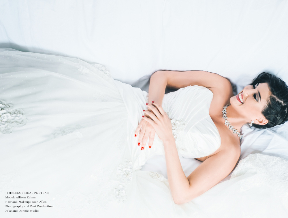 A bride laughs as she reclines on a big white bed.