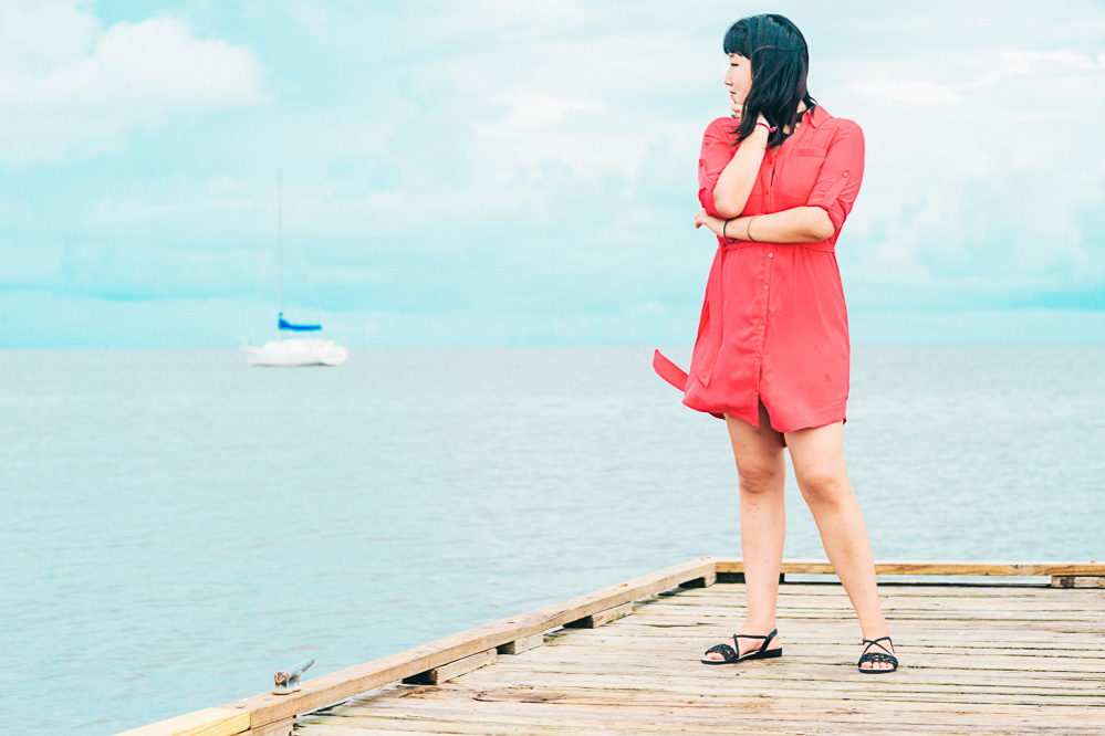 Dannie poses on a dock in her pink dress while a boat passes out at sea.